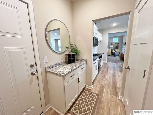 interior space with stainless steel range with gas cooktop, white cabinetry, light hardwood / wood-style flooring, and light stone counters