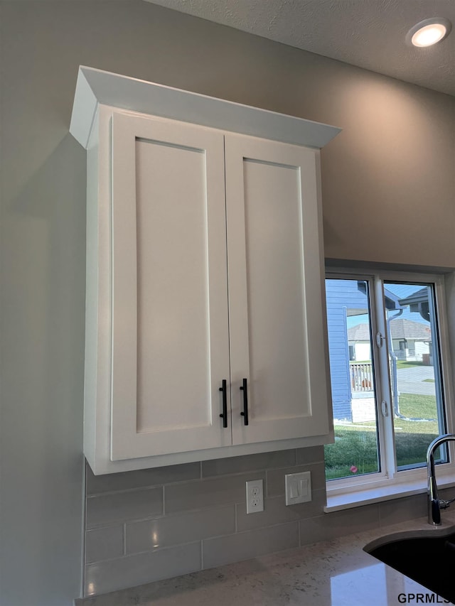 interior details with white cabinetry, sink, tasteful backsplash, light stone counters, and a textured ceiling