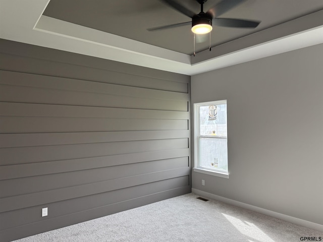 carpeted empty room with a raised ceiling and ceiling fan