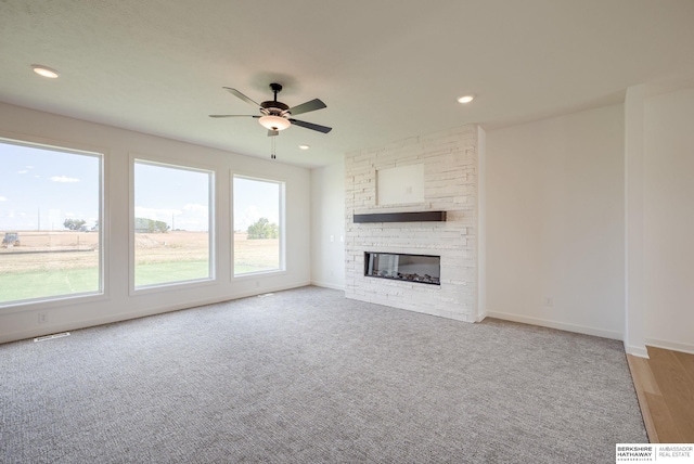 unfurnished living room featuring ceiling fan, a fireplace, light colored carpet, and plenty of natural light