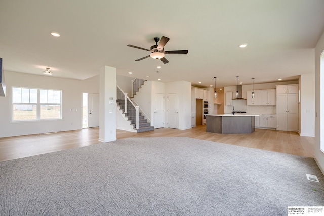 unfurnished living room with ceiling fan, sink, and light wood-type flooring