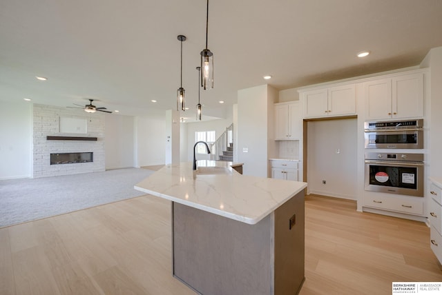 kitchen with white cabinetry, light stone countertops, hanging light fixtures, a brick fireplace, and a kitchen island with sink