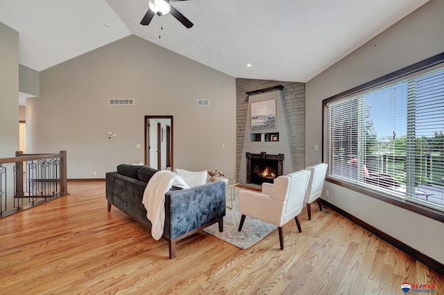 living room featuring vaulted ceiling, light hardwood / wood-style floors, a stone fireplace, and ceiling fan