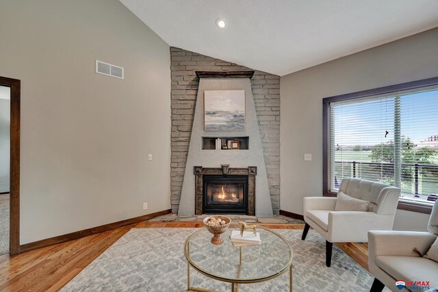 living room with a large fireplace, plenty of natural light, hardwood / wood-style floors, and lofted ceiling