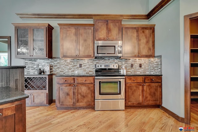 kitchen featuring decorative backsplash, dark stone counters, stainless steel appliances, crown molding, and light hardwood / wood-style floors