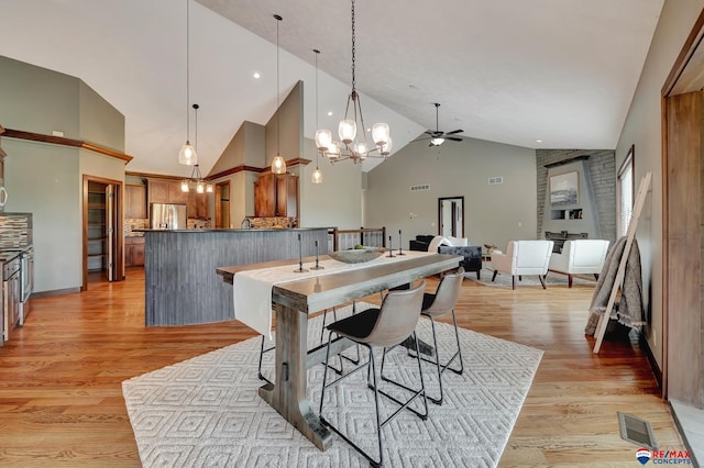 dining area with ceiling fan with notable chandelier, light hardwood / wood-style floors, and high vaulted ceiling