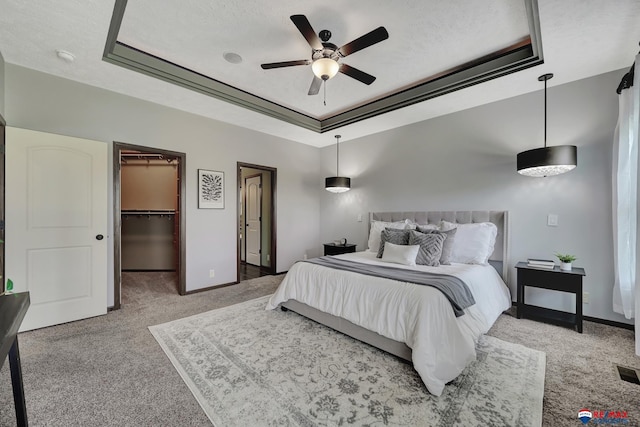 carpeted bedroom featuring a closet, a tray ceiling, a spacious closet, and ceiling fan