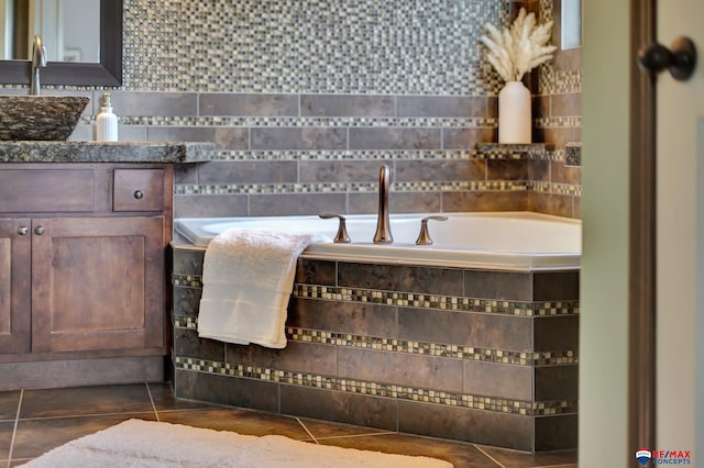 bathroom with tile patterned flooring, tiled bath, and sink