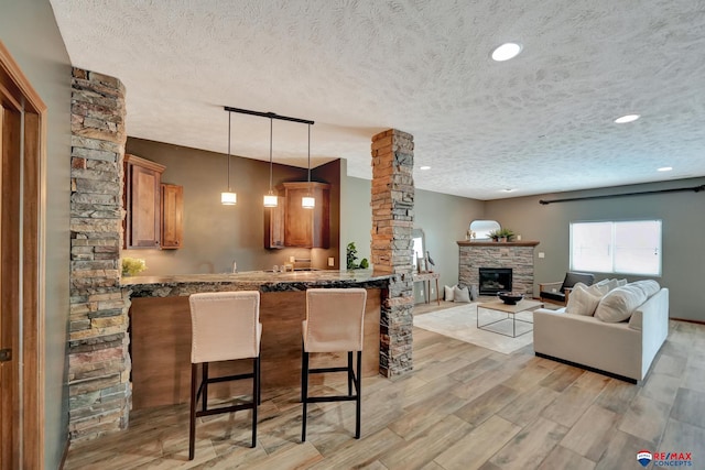 kitchen with kitchen peninsula, a kitchen breakfast bar, a textured ceiling, a fireplace, and hanging light fixtures