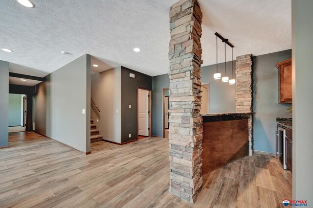 interior space with a textured ceiling, decorative light fixtures, beverage cooler, and stone countertops