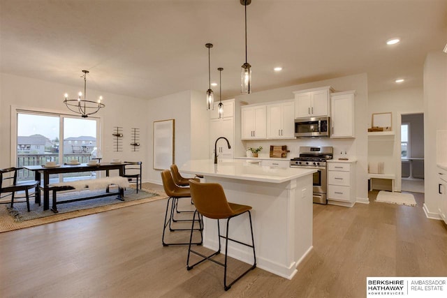 kitchen with stainless steel appliances, a kitchen island with sink, an inviting chandelier, white cabinetry, and hanging light fixtures