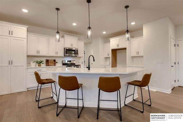 kitchen with white cabinetry, stainless steel appliances, and an island with sink