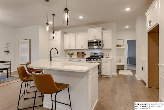 kitchen with a kitchen island with sink, white cabinets, hanging light fixtures, sink, and stainless steel appliances