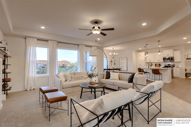 living room featuring a tray ceiling, sink, ceiling fan with notable chandelier, and light wood-type flooring