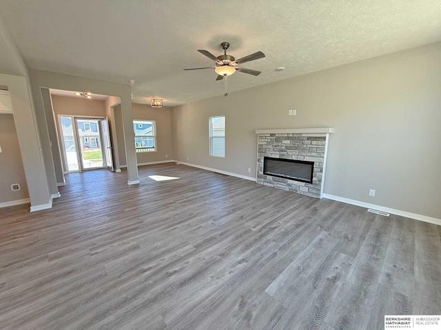 unfurnished living room featuring ceiling fan, a fireplace, a textured ceiling, and light wood-type flooring