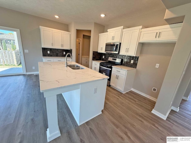 kitchen with sink, light stone counters, a center island with sink, white cabinets, and appliances with stainless steel finishes