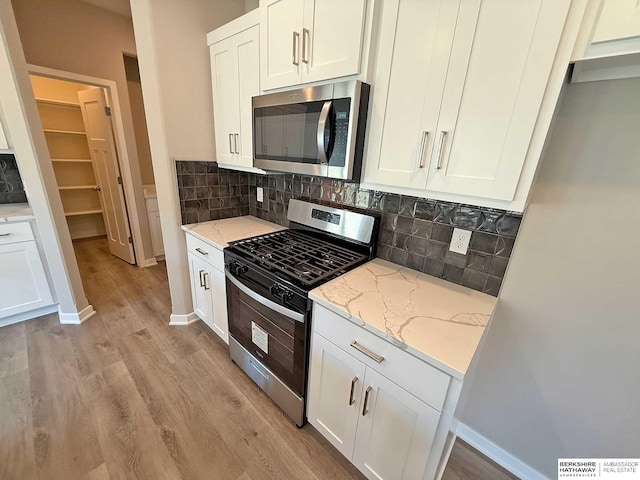 kitchen featuring light stone countertops, tasteful backsplash, light hardwood / wood-style floors, white cabinetry, and stainless steel appliances