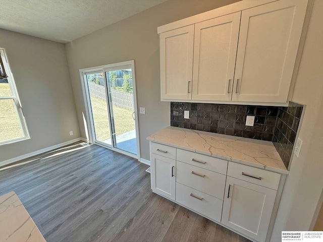 kitchen featuring white cabinetry, tasteful backsplash, light stone counters, light hardwood / wood-style flooring, and a textured ceiling