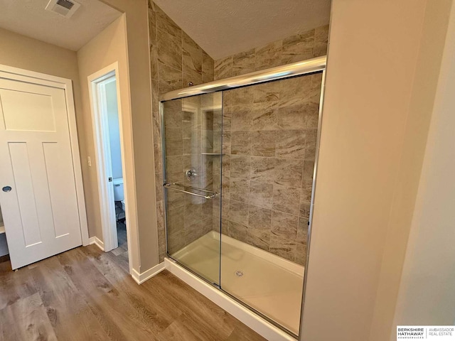 bathroom with a textured ceiling, hardwood / wood-style floors, an enclosed shower, and toilet