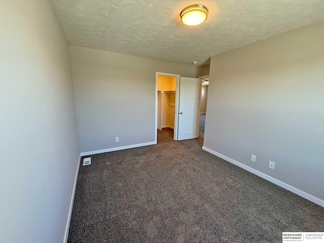 unfurnished bedroom with a walk in closet, a closet, a textured ceiling, and dark colored carpet