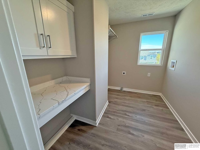 clothes washing area featuring cabinets, wood-type flooring, a textured ceiling, and hookup for a washing machine