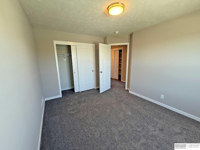 unfurnished bedroom with dark carpet, a textured ceiling, and a closet