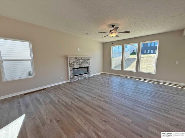 unfurnished living room featuring a stone fireplace, ceiling fan, wood-type flooring, and a textured ceiling