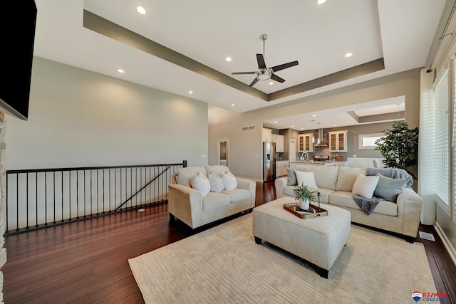 living room with hardwood / wood-style flooring, ceiling fan, a raised ceiling, and sink