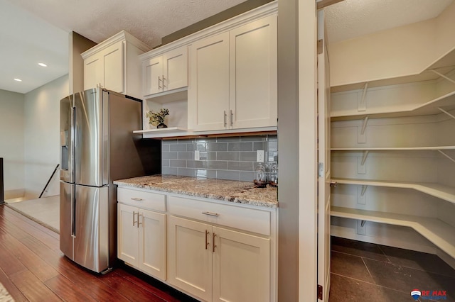 kitchen featuring light stone countertops, stainless steel refrigerator with ice dispenser, tasteful backsplash, and white cabinetry