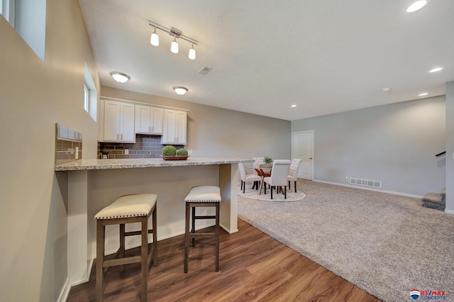 kitchen with backsplash, wood-type flooring, kitchen peninsula, white cabinetry, and a breakfast bar area