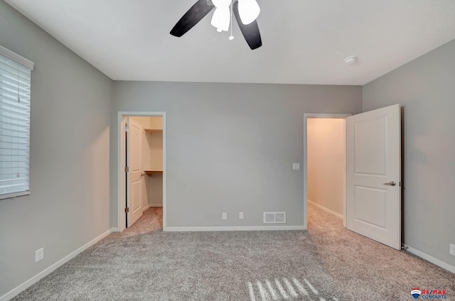 unfurnished bedroom featuring a walk in closet, a closet, ceiling fan, and light colored carpet