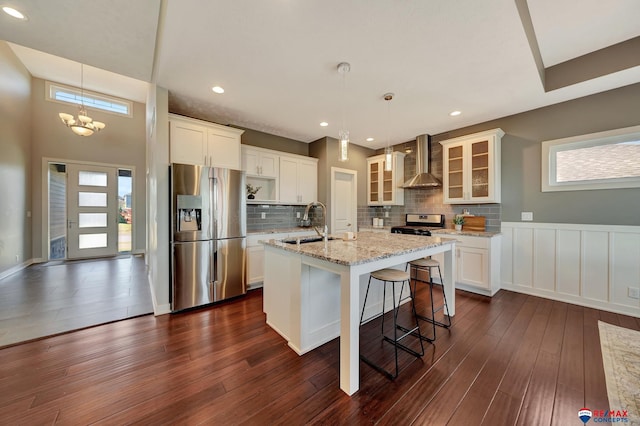 kitchen with a kitchen island with sink, sink, wall chimney exhaust hood, appliances with stainless steel finishes, and decorative light fixtures