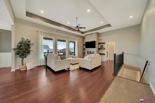 living room with dark hardwood / wood-style flooring, a tray ceiling, and ceiling fan