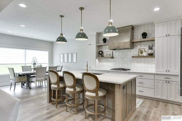 kitchen featuring sink, premium range hood, a kitchen island with sink, and hanging light fixtures