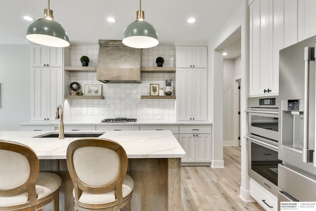 kitchen with light stone countertops, appliances with stainless steel finishes, white cabinetry, and custom range hood