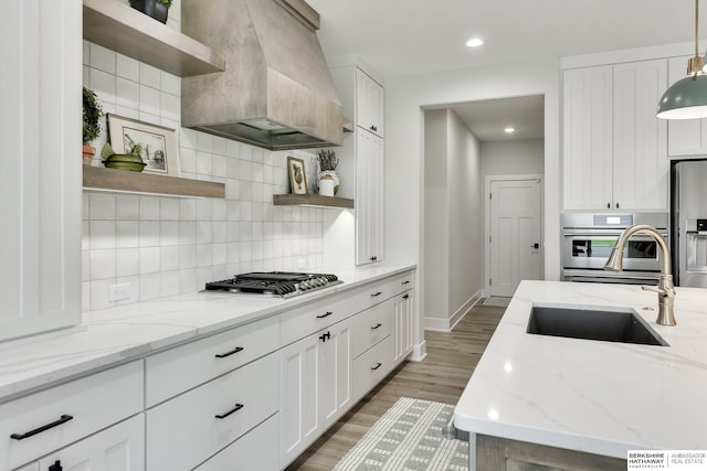 kitchen featuring custom exhaust hood, sink, light stone countertops, and stainless steel appliances