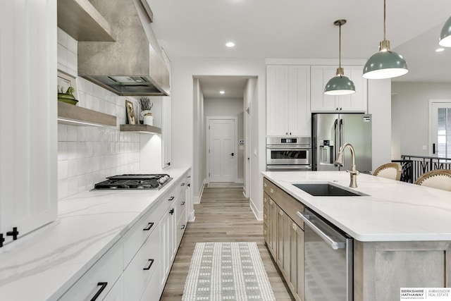 kitchen with white cabinetry, stainless steel appliances, light stone counters, premium range hood, and a center island with sink