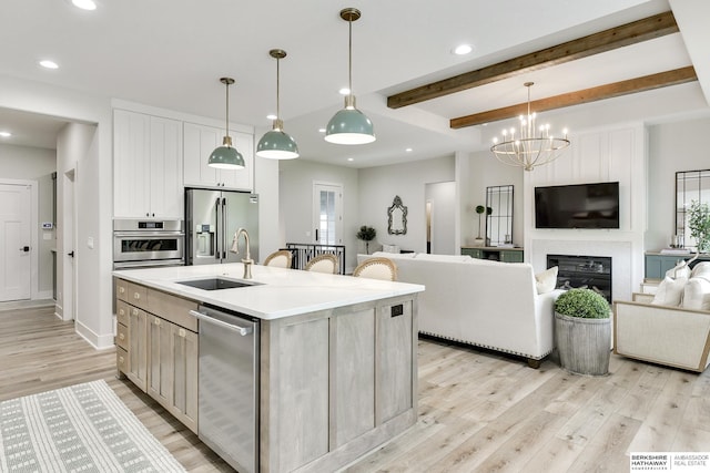 kitchen with a center island with sink, pendant lighting, beamed ceiling, and stainless steel appliances