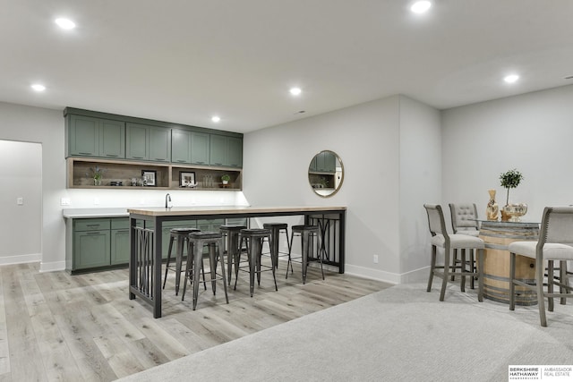 kitchen with a kitchen bar, decorative backsplash, light hardwood / wood-style flooring, and green cabinets