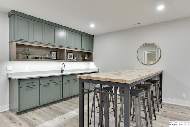 kitchen with backsplash, green cabinets, sink, and light hardwood / wood-style flooring