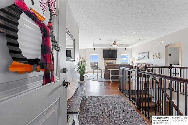 hallway with hardwood / wood-style floors, a textured ceiling, and a tray ceiling