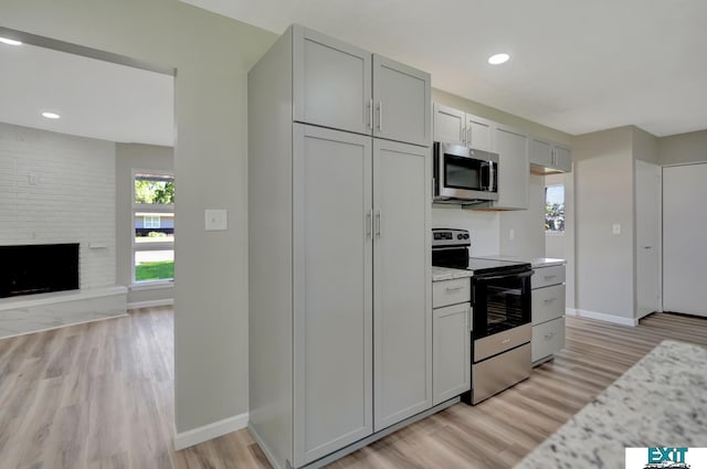 kitchen with a large fireplace, stainless steel appliances, light hardwood / wood-style flooring, and gray cabinetry