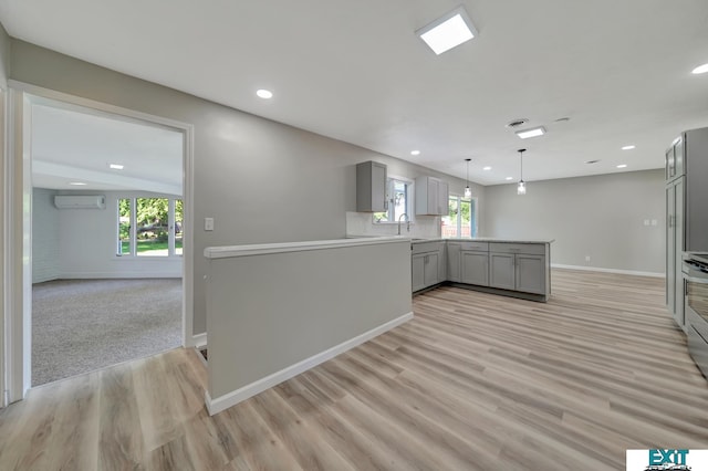 kitchen featuring kitchen peninsula, gray cabinets, a wall unit AC, and light hardwood / wood-style floors