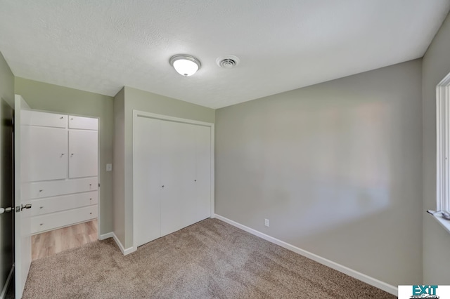 unfurnished bedroom with light colored carpet, a textured ceiling, and a closet