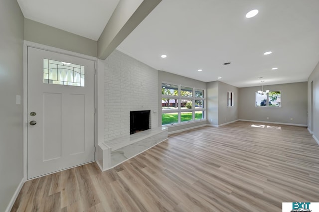 interior space featuring a wealth of natural light, light wood-type flooring, a notable chandelier, and a brick fireplace