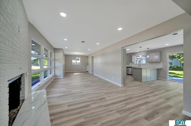 unfurnished living room with light wood-type flooring, sink, and a brick fireplace