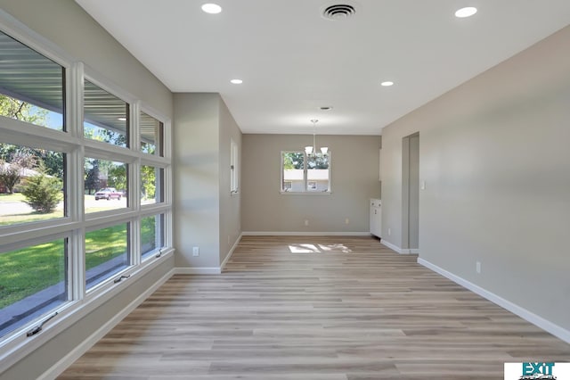 unfurnished room featuring a notable chandelier and light hardwood / wood-style flooring