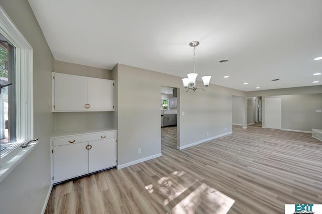 unfurnished dining area with a notable chandelier and light wood-type flooring