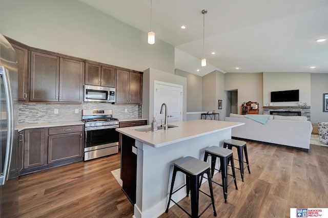 kitchen with a breakfast bar, hanging light fixtures, an island with sink, dark brown cabinets, and stainless steel appliances