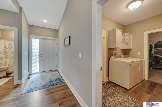 laundry area with washing machine and clothes dryer, dark wood-type flooring, and cabinets